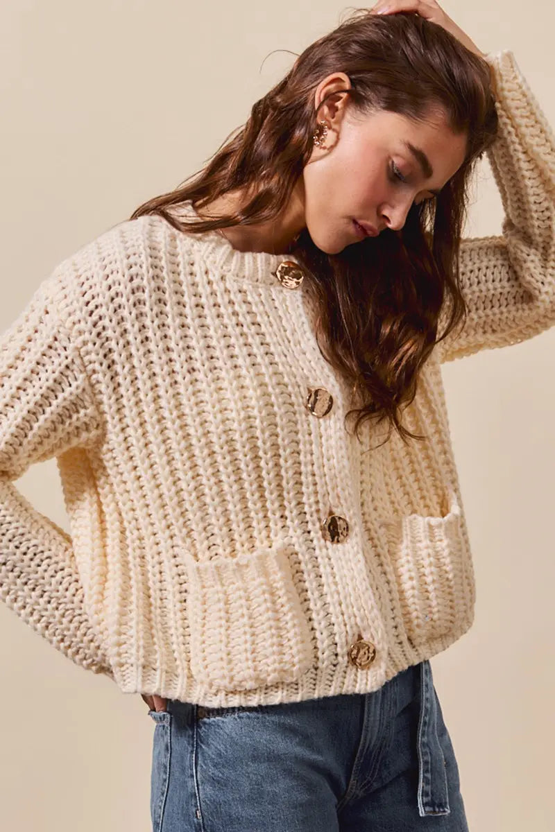 Cream-colored chunky knit cardigan with gold buttons and pockets