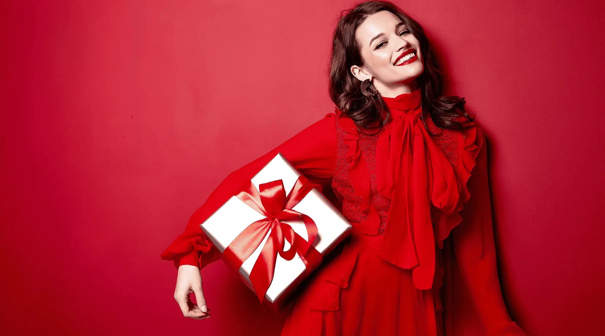 A woman smiling in a red dress, holding a wrapped gift.