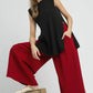 Woman wearing a black sleeveless top and red pants sitting on a wooden block against a gray background.