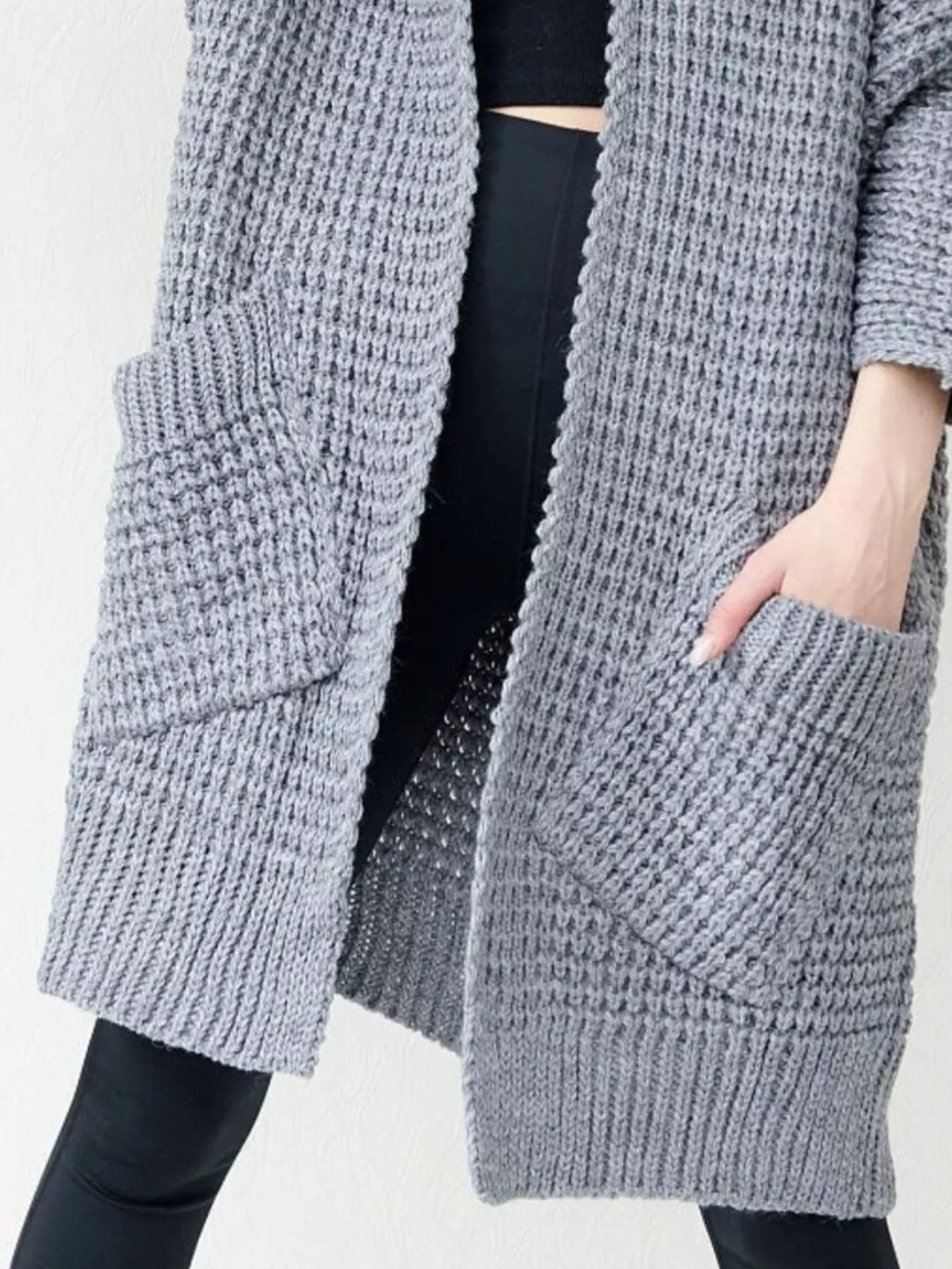 Woman wearing a cozy, longline gray chunky knit open-front cardigan with a textured waffle weave and large front pockets.