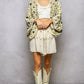 Woman in POL crochet floral cardigan and cream fringed mini skirt