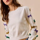 White SO ME Mardi Gras knit sweater with colorful sequined bows on sleeves