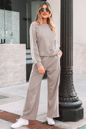 Woman in a gray tracksuit standing outdoors near a building entrance.