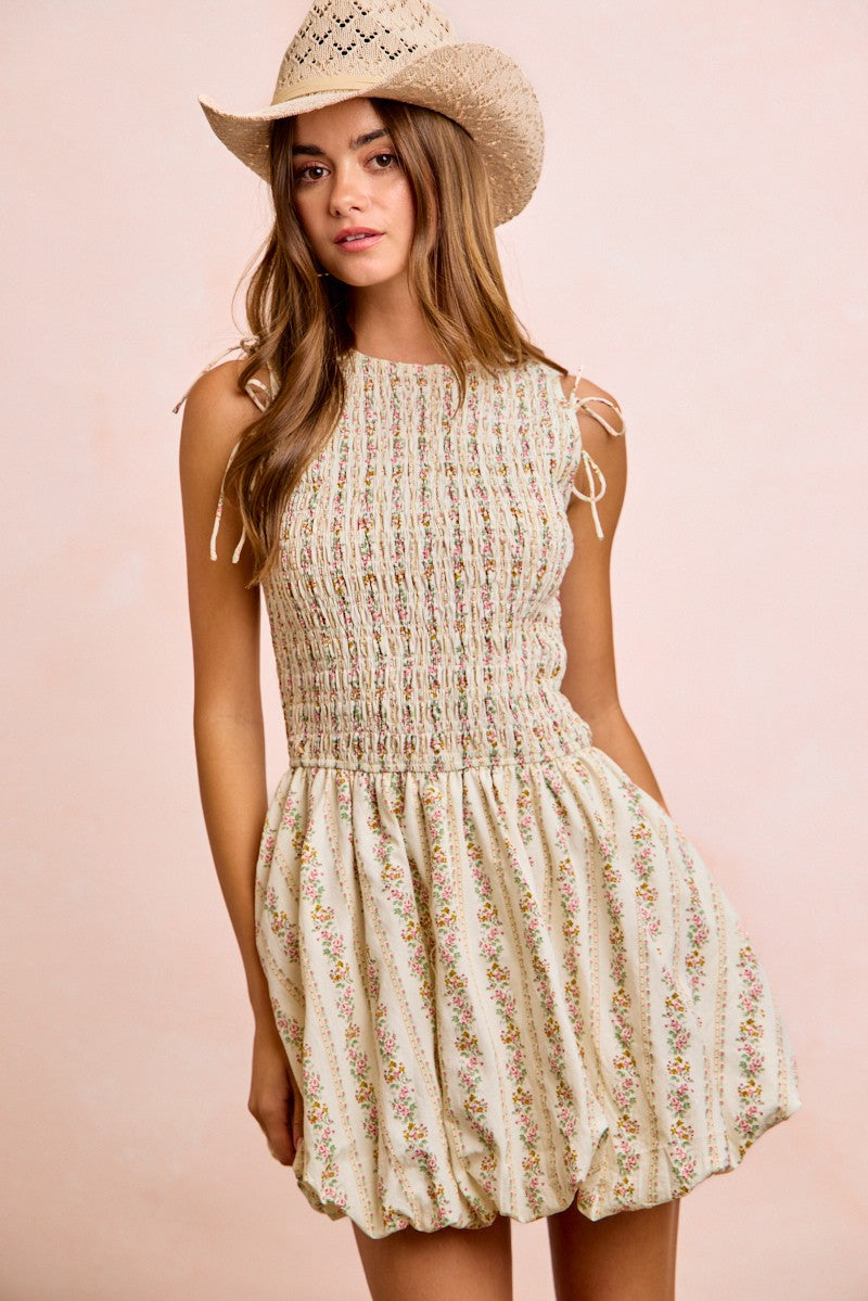 A sleeveless, cream-colored dress with a floral pattern and smocked bodice.