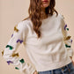 Cream-colored knit sweater with Mardi Gras sequined bows on sleeves