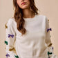 White knit sweater with colorful sequined bows in gold, purple, green