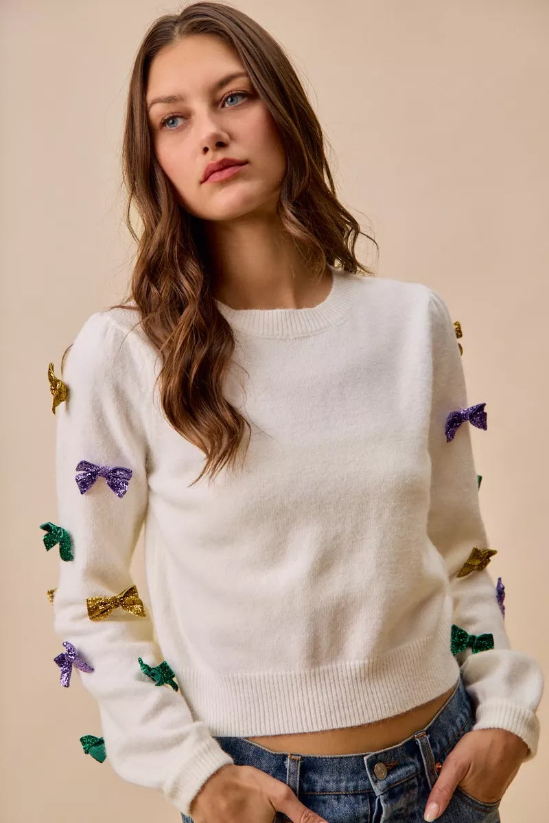 White knit sweater with colorful sequined bows in gold, purple, green