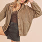 Woman wearing a brown corduroy jacket over a black top and denim shorts on a beige background