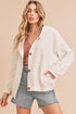 Woman wearing a white jacket over a pink top and denim shorts on a beige background