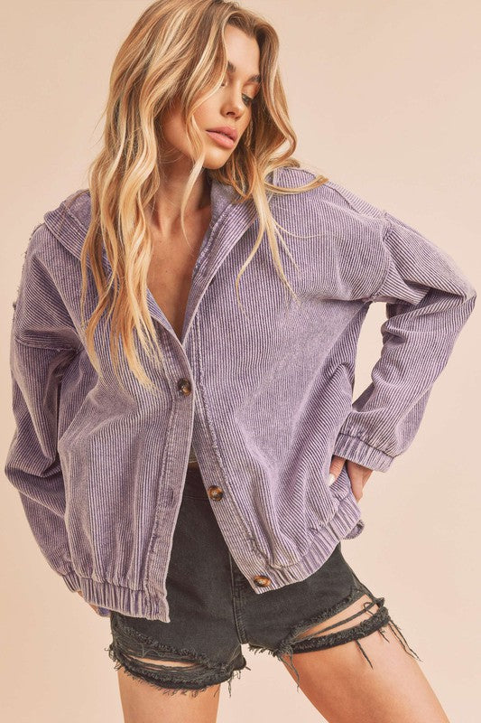 Woman wearing a purple corduroy jacket and black shorts on a beige background