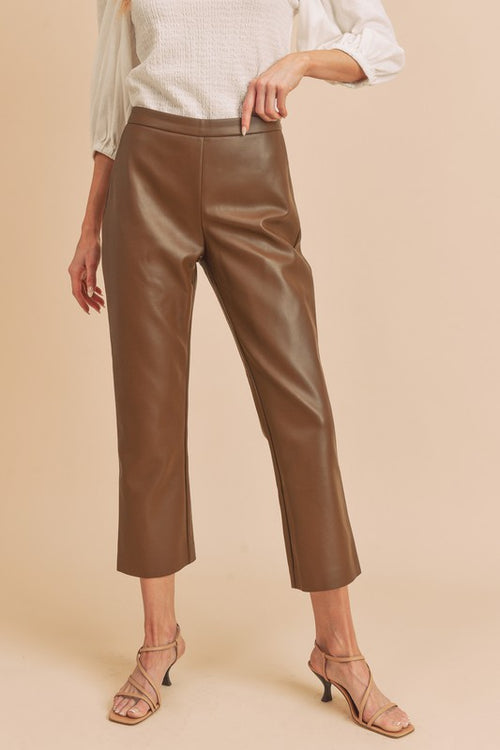 Person wearing brown leather pants on a beige background
