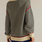 Black and cream striped knit sweater with red trim on sleeves, hem, and cuffs