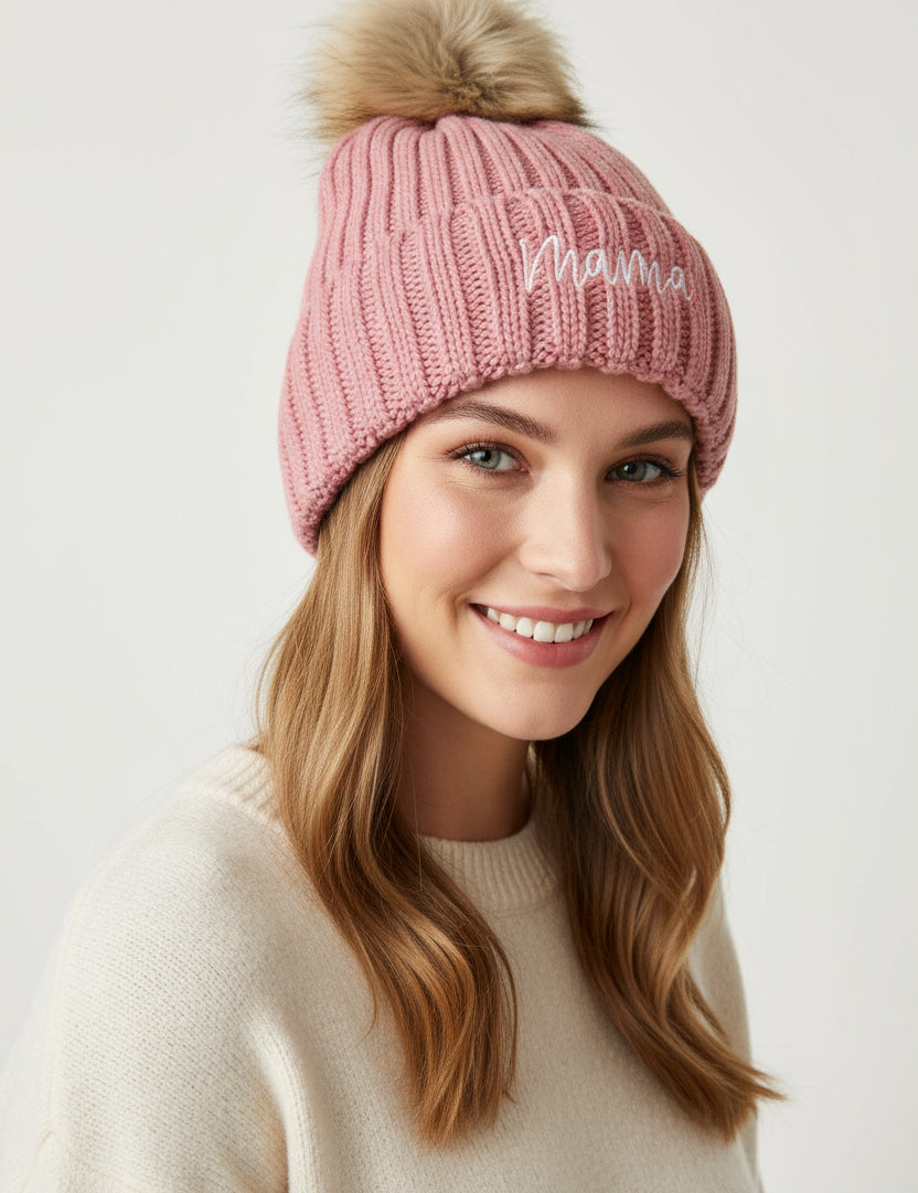 Pink knit beanie with fur pom-pom on a textured surface
