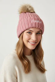 Pink knit beanie with fur pom-pom on a textured surface