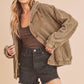 Woman wearing a brown corduroy jacket over a brown top and black shorts on a beige background