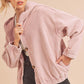 Woman wearing a pink corduroy jacket and black shorts on a beige background