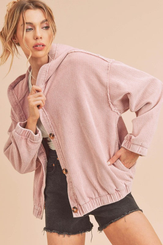Woman wearing a pink corduroy jacket and black shorts on a beige background