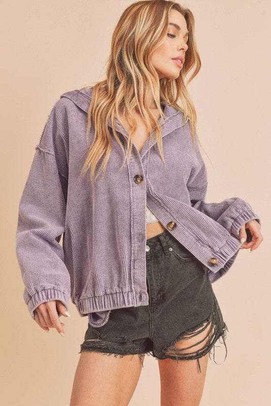 Woman wearing a purple corduroy jacket and black shorts on a beige background