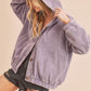 Woman wearing a purple corduroy jacket with a hood against a beige background
