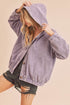 Woman wearing a purple corduroy jacket with a hood against a beige background