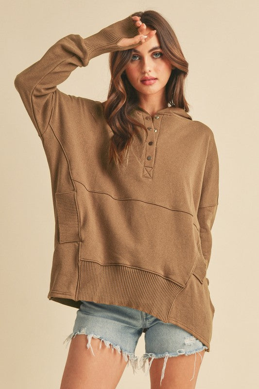 Woman wearing a brown hoodie and denim shorts against a beige background
