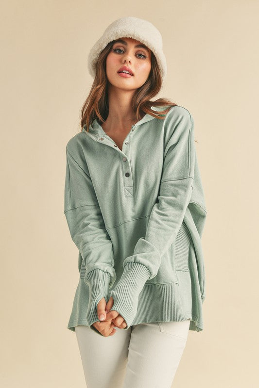 Woman wearing a light green hoodie and white pants on a beige background