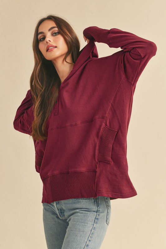 Woman wearing a burgundy hoodie and light blue jeans on a beige background