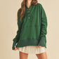 Woman wearing a green long-sleeve hoodie over a white dress on a beige background