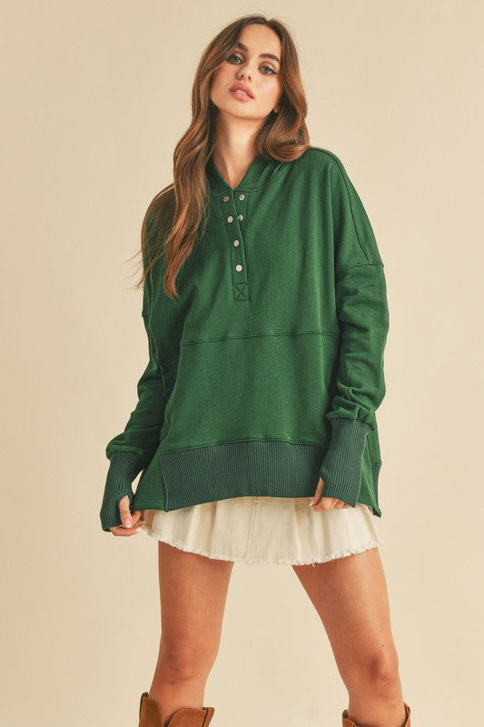 Woman wearing a green long-sleeve hoodie over a white dress on a beige background