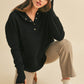Woman wearing a black long-sleeve hoodie, beige pants, and brown shoes on a beige background