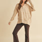Woman wearing a beige long-sleeve hoodie, brown pants, and a patterned hat on a beige background