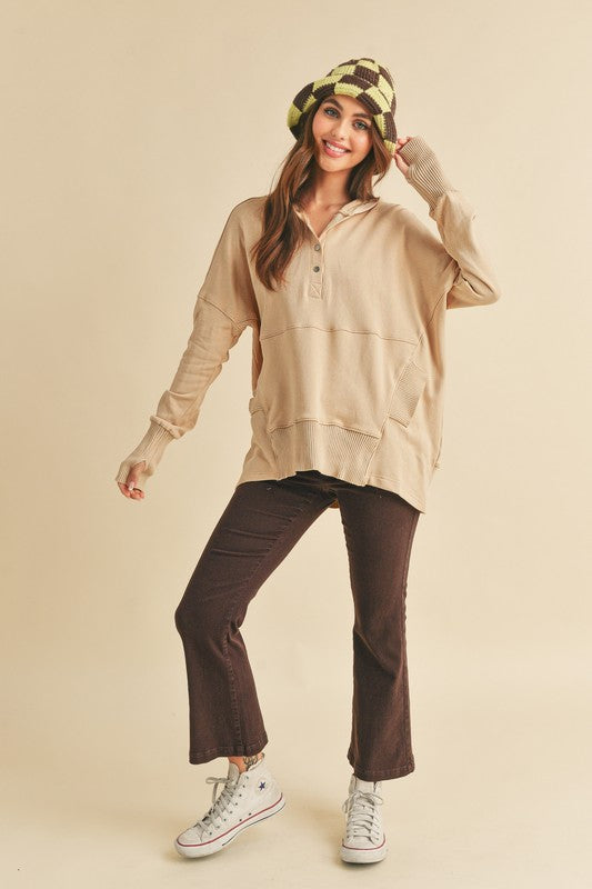 Woman wearing a beige long-sleeve hoodie, brown pants, and a patterned hat on a beige background