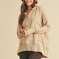 Woman wearing a beige long-sleeve hoodie, brown pants, and a patterned hat on a beige background