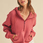 Woman wearing a pink hoodie and white pants against a beige background