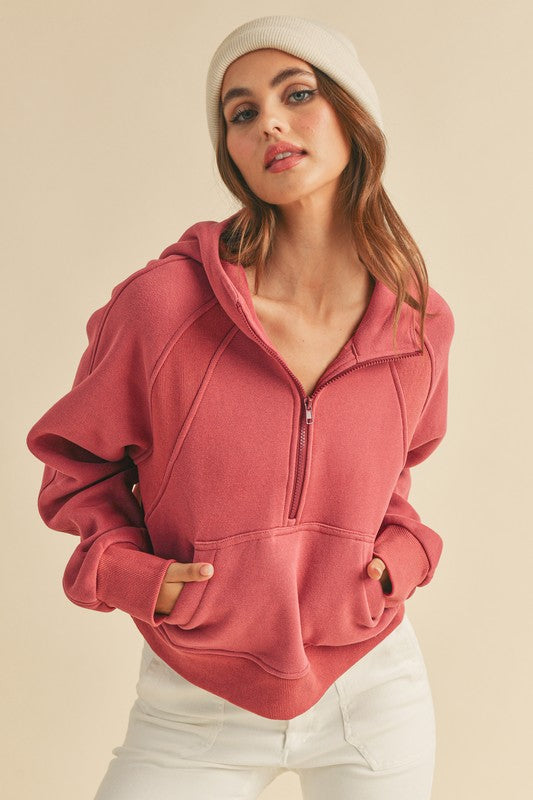 Woman wearing a pink hoodie and white pants against a beige background