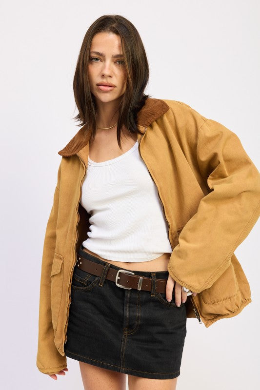 Woman wearing a tan jacket over a white top and black skirt on a white background