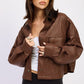 Woman wearing a brown textured jacket over a white top and black shorts on a light gray background