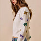 White knit sweater with colorful sequined bows in gold, purple, green