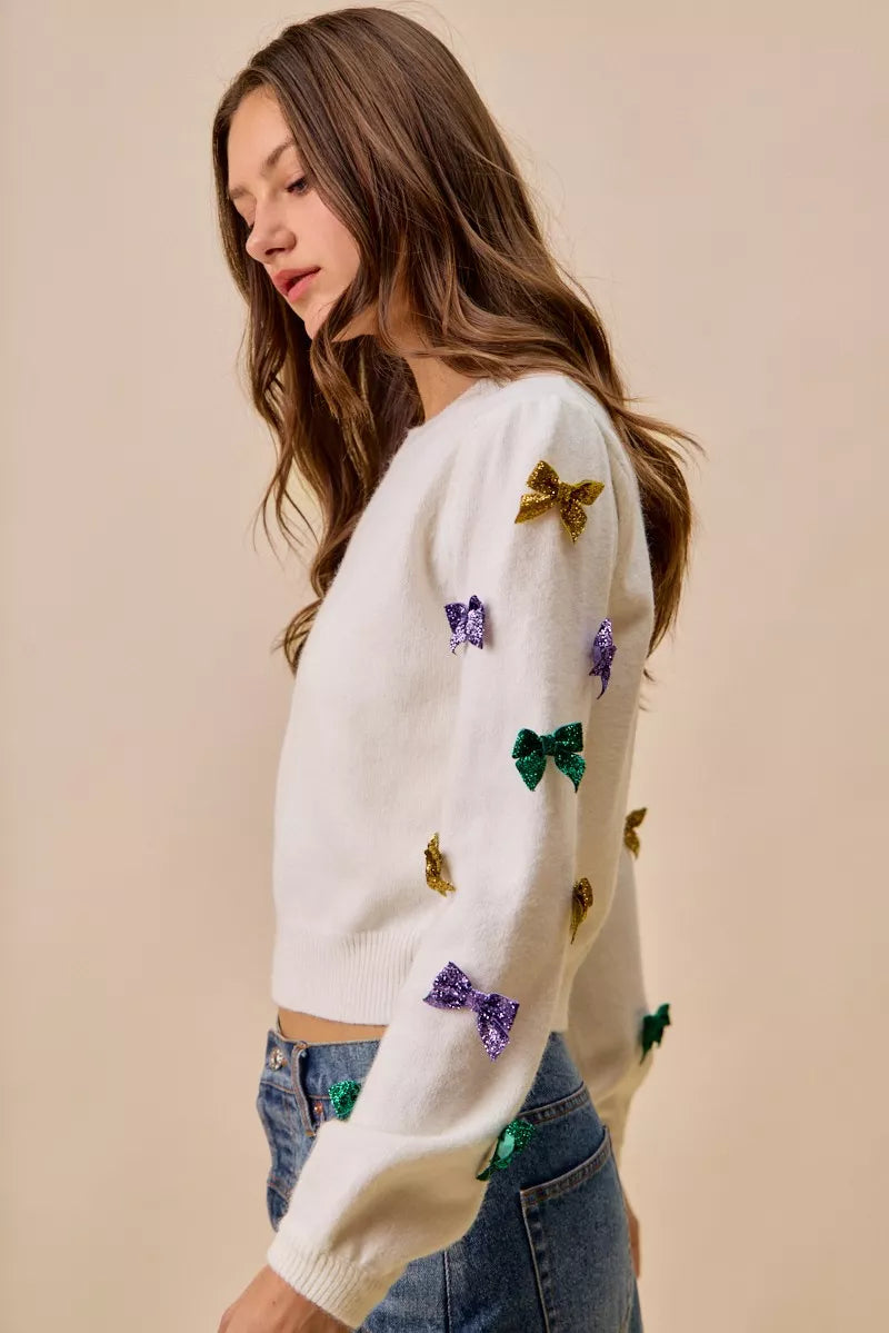 White knit sweater with colorful sequined bows in gold, purple, green