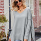 Light gray oversized V-neck knit sweater with ribbed cuffs and exposed seams