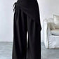 Daverri wrap-front wide-leg pants in black with draped asymmetrical design and side tie detail