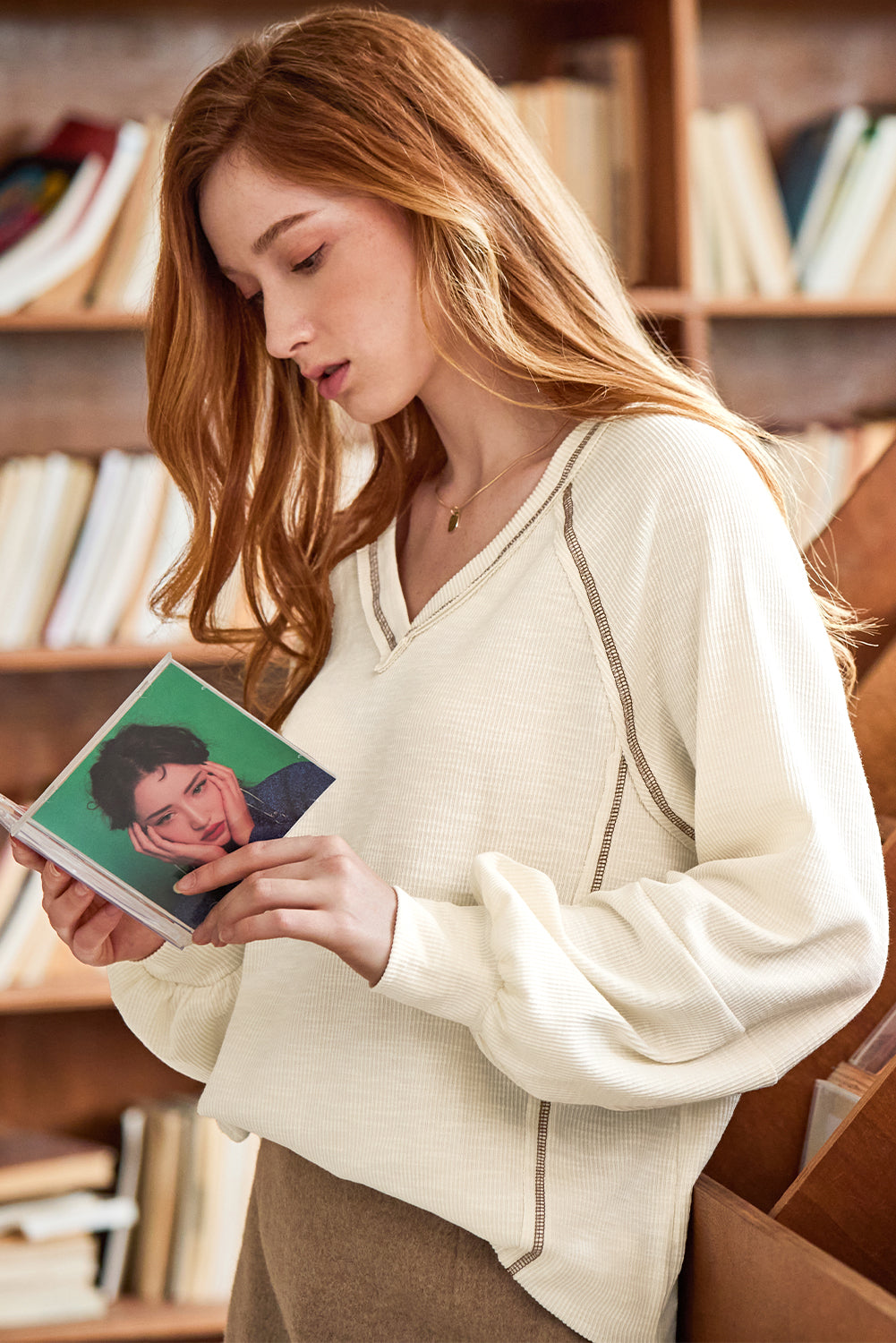 Cream-colored ribbed knit V-neck pullover with exposed seam stitching