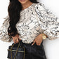 Black quilted handbag with gold chain strap on beige abstract print blouse
