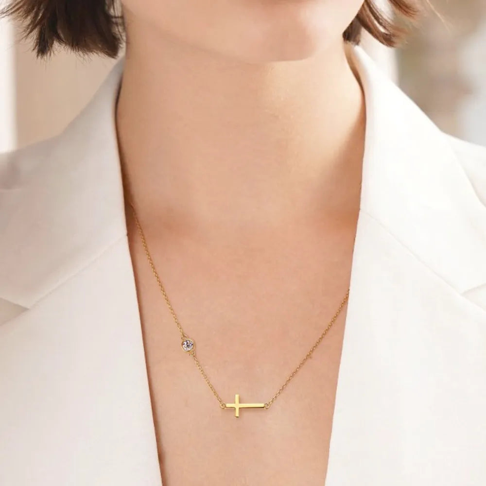 Gold necklace with a cross pendant and round moissanite stone on a person wearing a white outfit.