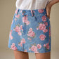 Floral print denim mini skirt with pink rose pattern on blue background