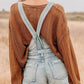 Distressed denim overalls shorts with light-wash frayed hem over brown sweater