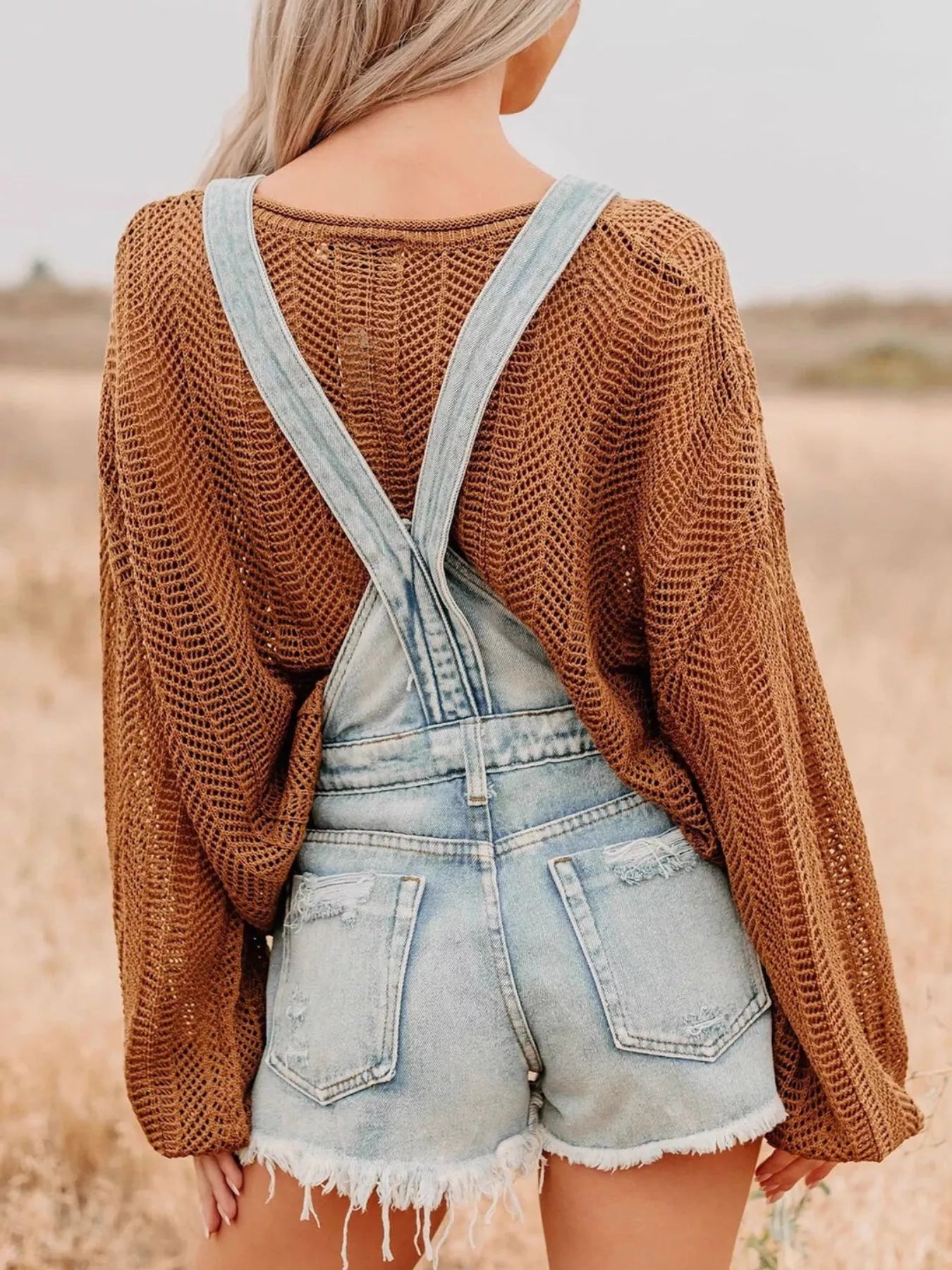 Distressed denim overalls shorts with light-wash frayed hem over brown sweater