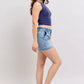 Woman in Judy Blue mid-rise light-wash denim shorts, navy crop top, tan sandals