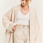 A woman wearing a longline beige oversized cardigan and shorts top