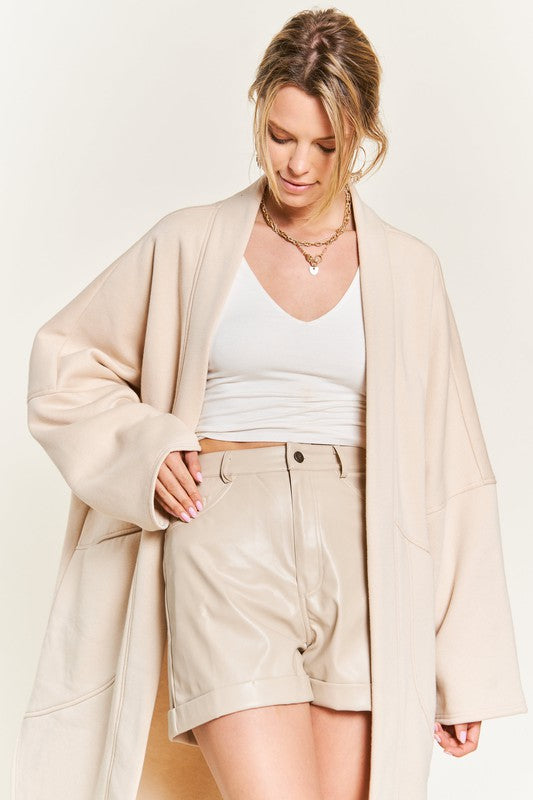 A woman wearing a longline beige oversized cardigan and shorts top